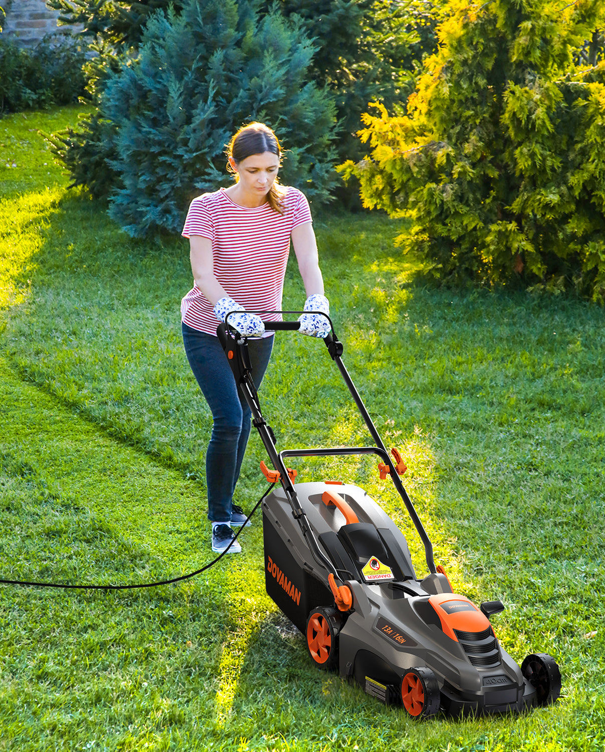 A woman using a DOVAMAN lawn mower on a grassy area with trees in the background